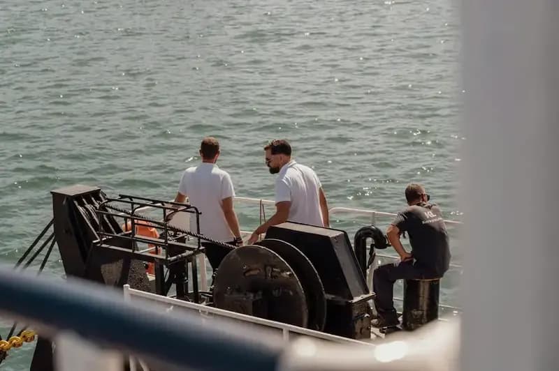 Three crew members on deck looking out to sea